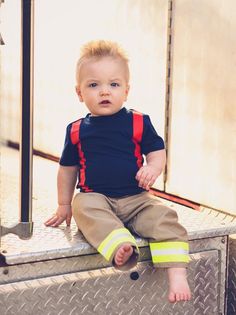 a little boy sitting on the back of a truck with his fireman's gear