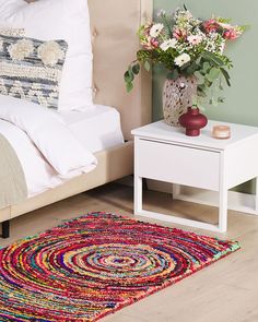 a colorful rug on the floor next to a bed with pillows and flowers in a vase