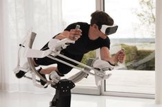 a man sitting in a chair holding a remote control and looking at the screen while wearing virtual reality glasses