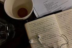 an open book sitting on top of a table next to a cup of coffee and headphones