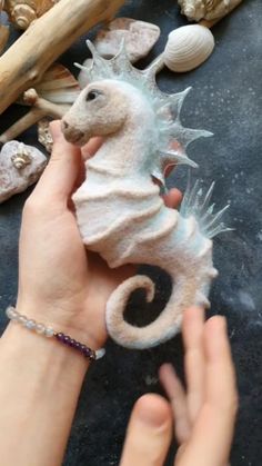 a person holding a sea horse toy in their hand next to shells and seashells