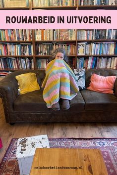 a woman wrapped in a blanket sitting on a couch with bookshelves behind her