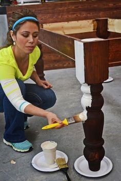 a woman kneeling down to paint a table with a brush and cup on the ground