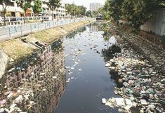 there are many trash floating in the water next to the road and buildings on the other side