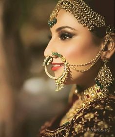 a woman wearing gold jewelry and an elaborate head piece with jewels on her face, looking into the distance