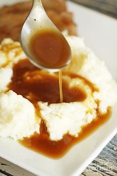 a spoon drizzling sauce over mashed potatoes and gravy on a white plate