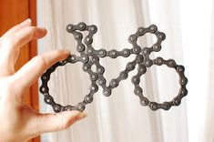 a person holding up an object made out of bicycle chain links in front of a window