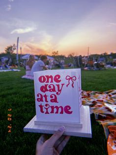 someone is holding up a card that says one day at a time on the grass