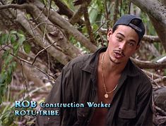 a young man is standing in the woods wearing a hat and looking at the camera