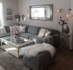 a living room with gray couches and white fur rugs on the floor in front of a large mirror