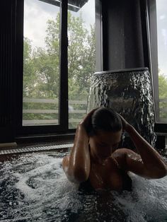 a woman in a hot tub with trees out the window and water running down it