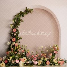 an arch decorated with flowers and greenery on top of a table in front of a wall