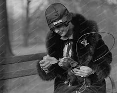 a woman sitting on a park bench holding a small animal in her hands and wearing a hat