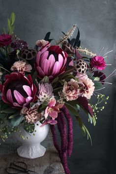 a white vase filled with lots of flowers on top of a wooden table next to scissors