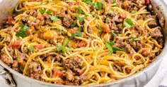 a large pot filled with spaghetti and meat on top of a white table cloth next to a fork