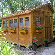 a small wooden building with windows and flower boxes on the outside, surrounded by greenery