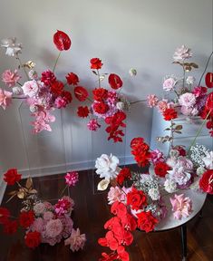 red and pink flowers are arranged in vases on a table next to a wall