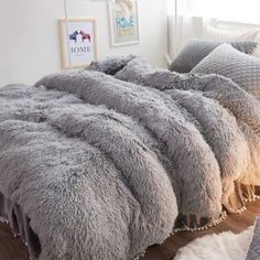 a bed covered in grey fluffy blankets and pillows