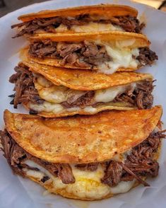 a white plate topped with three tacos covered in meat and cheese on top of tortillas