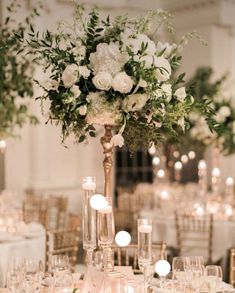 a tall vase filled with lots of white flowers and greenery on top of a table