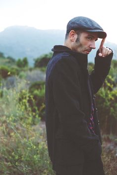 a man standing in the grass with his hand up to his face and wearing a hat