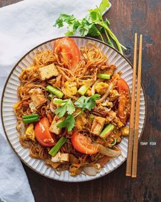 a plate full of noodles and vegetables with chopsticks next to it on a wooden table