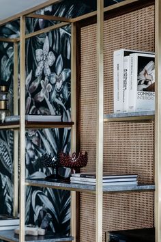 a book shelf with books on it in front of a floral wallpaper