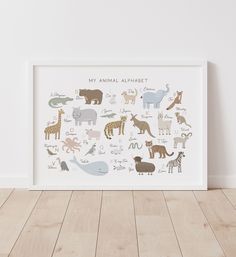 an animal alphabet is displayed in a white frame on a wooden floor next to a wall