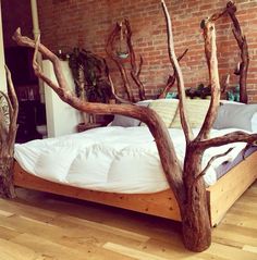 a bed made out of branches in a room with brick wall and hardwood flooring