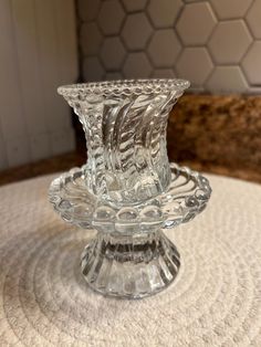 a clear glass candle holder sitting on top of a white tablecloth covered round table