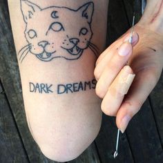 a person with a cat tattoo on their arm and the words dark dreams written in black ink