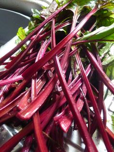 beets are piled up on top of each other in a bowl, with green leaves