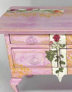 a pink and yellow dresser with flowers painted on the drawers is against a white background