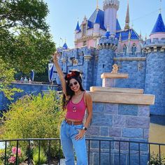 a woman standing in front of a castle with her hand up to the sky and smiling