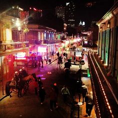 people walking down the street at night with lights on and buildings lit up in the background