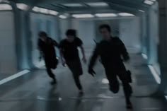 three young men are running down a hallway in the same direction, one is wearing black