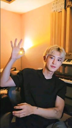 a young man sitting in front of a piano with his hand up to the camera