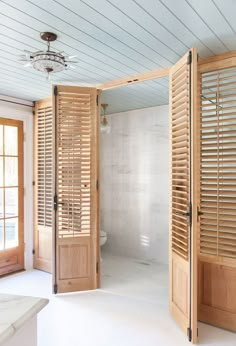 an open door leading to a bathroom with white walls and wood shutters on the doors