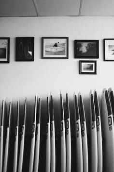 black and white photograph of surfboards in front of pictures on the wall above them