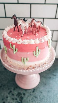 there is a cake with horses on top and cactus around the edges, sitting on a pedestal