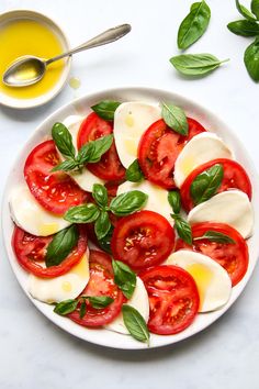 a white plate topped with sliced tomatoes and mozzarella cheese on top of green leaves