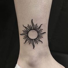 a black and white photo of a sun tattoo design on the side of a woman's ankle