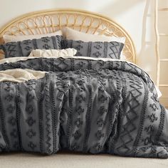 a bed with grey and white comforter on top of it next to a wicker headboard