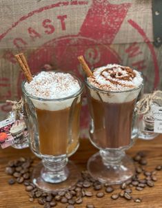 two glasses filled with hot chocolate and topped with whipped cream on top of coffee beans