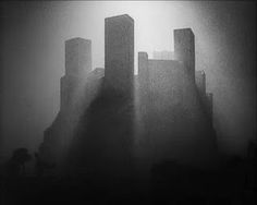 black and white photo of buildings in the foggy sky with light coming from behind