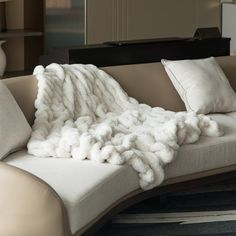 a large white blanket sitting on top of a couch next to pillows and a vase