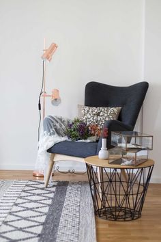 a living room with a chair, table and lamp on the floor in front of a white wall