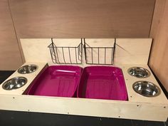 two pink dog bowls in a wooden crate