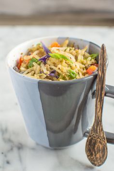 a cup filled with rice and vegetables next to a spoon