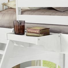 a white bunk bed with two books and a cup on the bottom shelf next to it